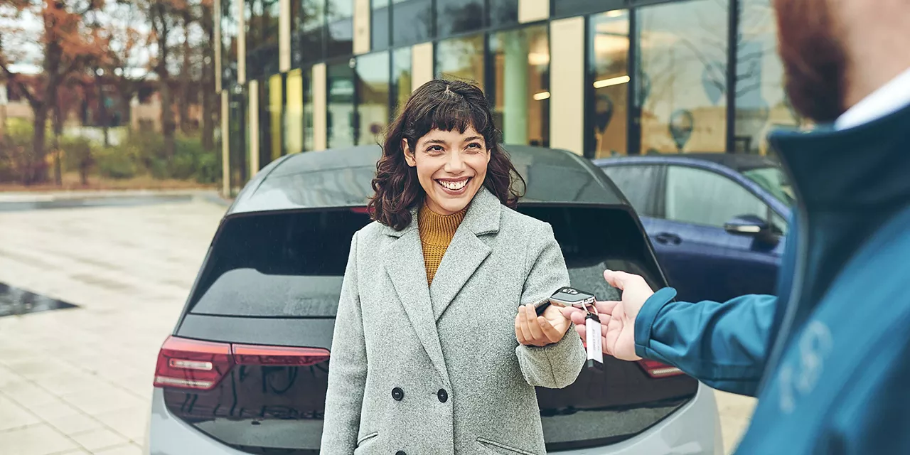 Vermietrepräsentant der Autovermietung VW FS | Rent-a-Car übergibt einer Kundin den Autoschlüssel