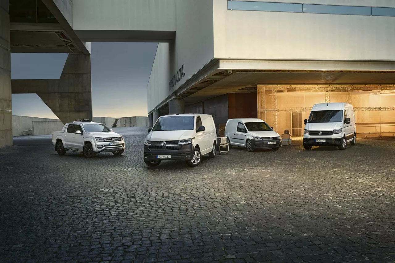 Verschiedene weiße Modelle von VW Nutzfahrzeuge stehen vor einer Lagerhalle